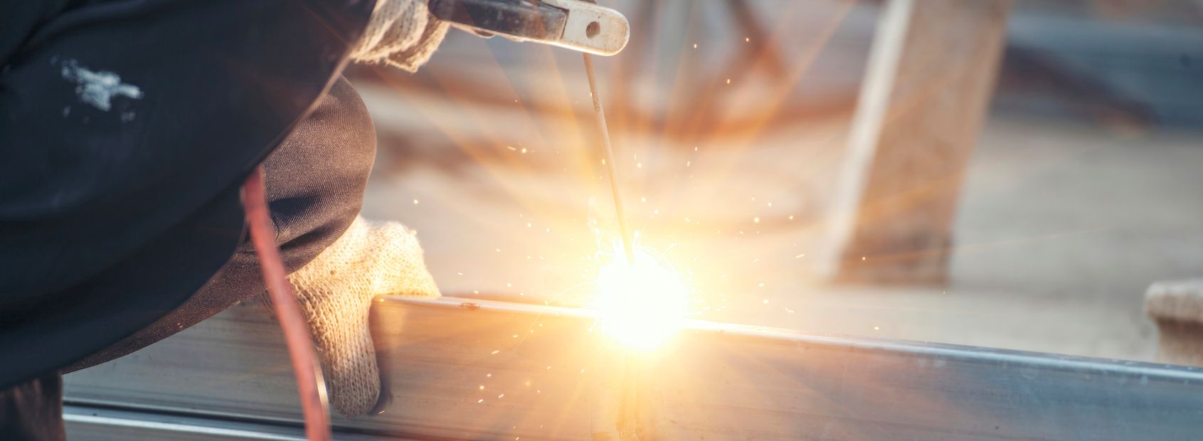 A close-up of a person welding metal, with bright sparks and light emitted from the welding point. The worker's gloved hands and part of their protective clothing are visible, showcasing the skill of a Welding Company Toowoomba professional.