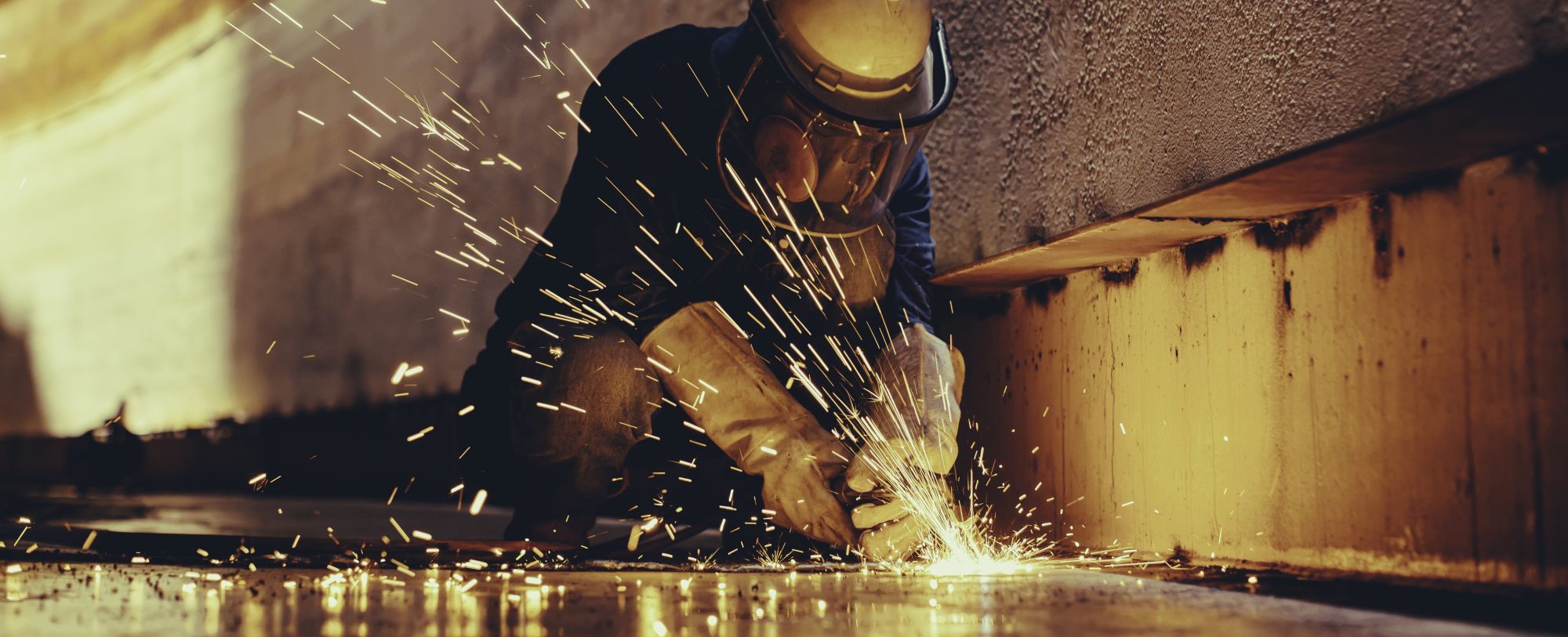 A worker wearing protective gear uses a grinder, producing bright sparks while working on a metal surface at a Welding Company Toowoomba industrial site.