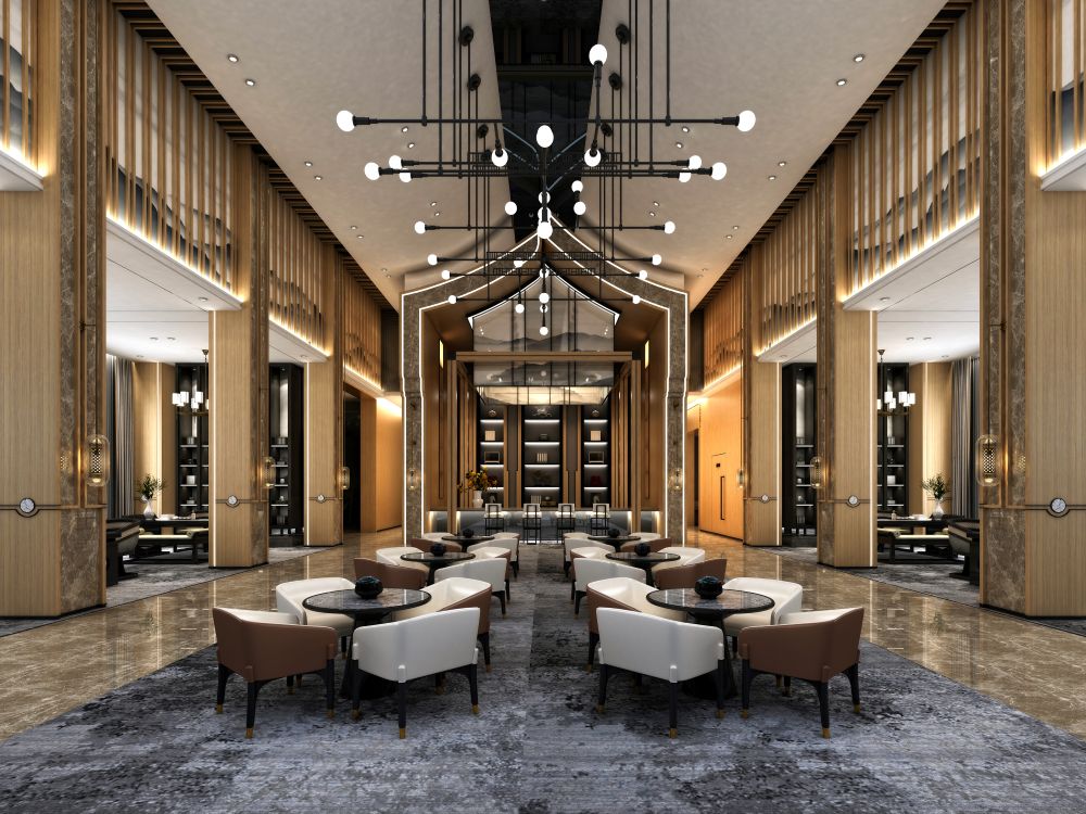 A spacious, modern hotel lobby with high ceilings, elegant lighting fixtures, plush armchairs around round tables, tall wooden panels, and a stylish shelving unit at the far end.